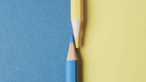 Overhead-view-of-yellow-and-blue-crayons-arranged-on-blue-and-yellow-background,-in-slow-motion