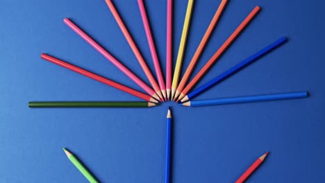 Overhead-view-of-crayons-arranged-on-blue-background,-in-slow-motion