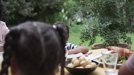 Happy-biracial-parents,-son-and-daughter-praying-before-meal-at-dinner-table-in-garden,-slow-motion