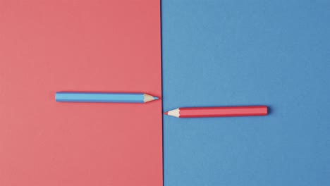 Overhead-view-of-blue-and-red-crayons-arranged-on-red-and-blue-background,-in-slow-motion