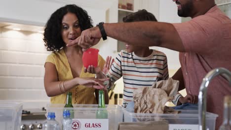 Happy-biracial-couple-with-daughter-and-son-segregating-waste-in-kitchen,-slow-motion