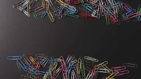 Overhead-view-of-scattered-colourful-paper-clips-with-copy-space-on-black-background,-in-slow-motion