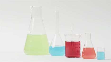 Coloured-liquids-in-flasks-on-white-background-with-copy-space,-slow-motion