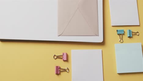 Overhead-view-of-notebook,-pens-and-stationery-arranged-on-yellow-background,-in-slow-motion