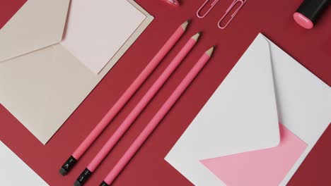 Overhead-view-of-pens,-pencils-and-stationery-arranged-on-red-background,-in-slow-motion