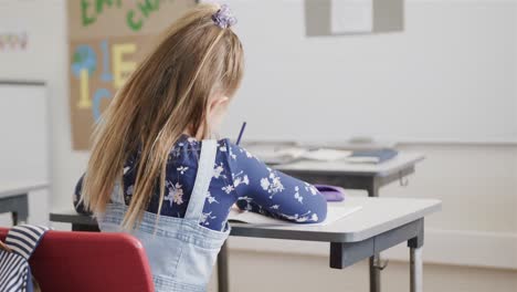 Rear-view-of-caucasian-schoolgirl-writing-at-desk-in-elementary-school-class,-slow-motion