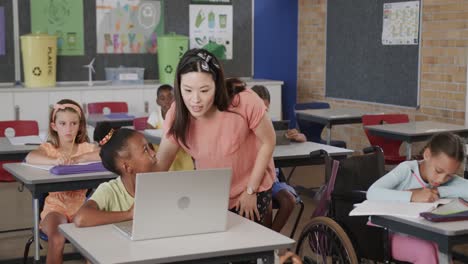 Fröhliche,-Vielfältige-Lehrerin-Hilft-Mädchen-Beim-Benutzen-Eines-Laptops-In-Der-Grundschulklasse,-Zeitlupe