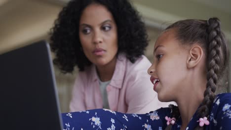 Happy-biracial-mother-and-daughter-learning-online-using-laptop-at-table,-slow-motion