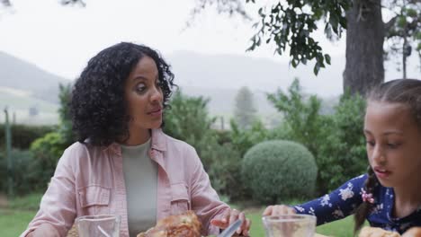 Happy-biracial-parents-and-daughter-eating-meal-at-dinner-table-in-garden,-slow-motion