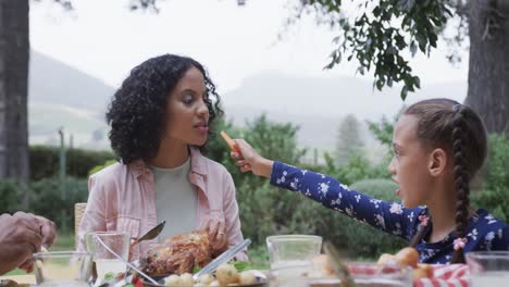 Happy-biracial-mother-and-daughter-eating-meal-at-dinner-table-in-garden,-slow-motion