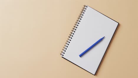 Overhead-view-of-blue-marker-on-notebook-with-copy-space-on-beige-background,-in-slow-motion