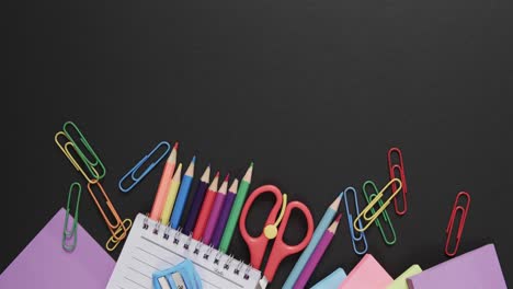 Overhead-view-of-colourful-school-stationery-with-copy-space-on-black-background,-in-slow-motion