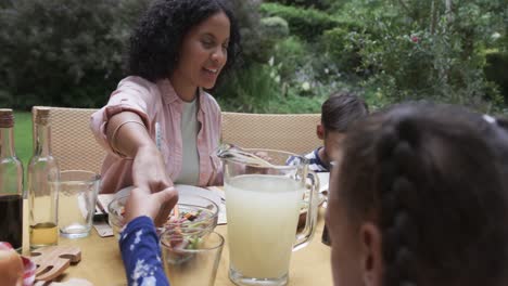 Happy-biracial-parents,-son-and-daughter-praying-at-dinner-table-in-garden,-slow-motion