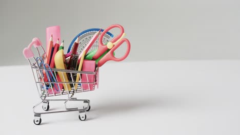 Close-up-of-shopping-trolley-with-school-items-and-copy-space-on-grey-background