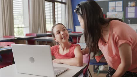Fröhliche,-Vielfältige-Lehrerin-Hilft-Mädchen-Beim-Benutzen-Eines-Laptops-In-Der-Grundschulklasse,-Zeitlupe