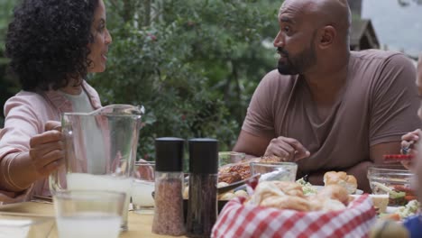 Happy-biracial-couple-enjoying-meal-and-talking-at-dinner-table-in-garden,-slow-motion