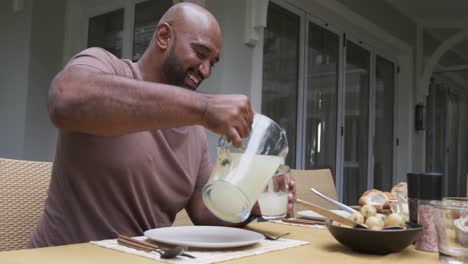 Happy-biracial-parents-and-son-serving-meal-at-dinner-table-in-garden,-slow-motion