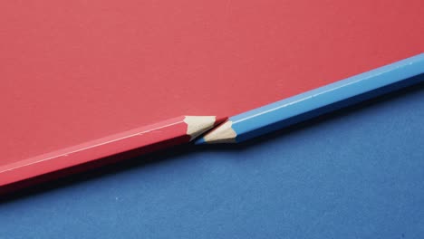 Overhead-view-of-blue-and-red-crayons-arranged-on-red-and-blue-background,-in-slow-motion