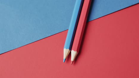 Overhead-view-of-blue-and-red-crayons-on-red-and-blue-background,-in-slow-motion