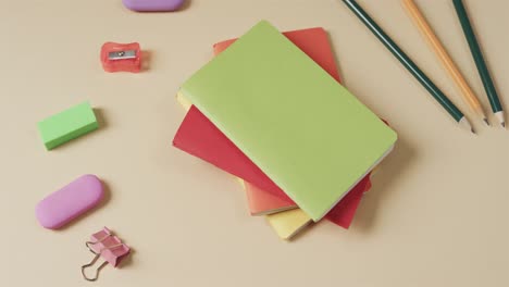 Close-up-of-colourful-notebooks-with-school-stationery-on-beige-background,-in-slow-motion