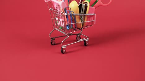 Close-up-of-shopping-trolley-with-school-items-with-copy-space-on-red-background