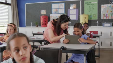 Happy-diverse-female-teacher-helping-girl-using-tablet-in-elementary-school-class,-slow-motion