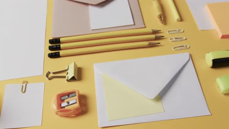 Close-up-of-pens,-pencils-and-stationery-arranged-on-yellow-background,-in-slow-motion