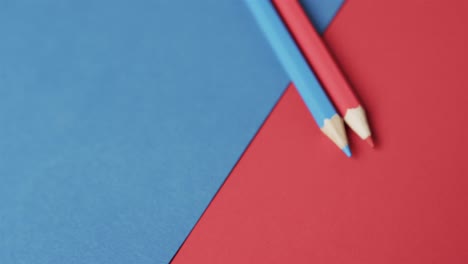 Close-up-of-blue-and-red-crayons-with-copy-space-on-red-and-blue-background,-in-slow-motion