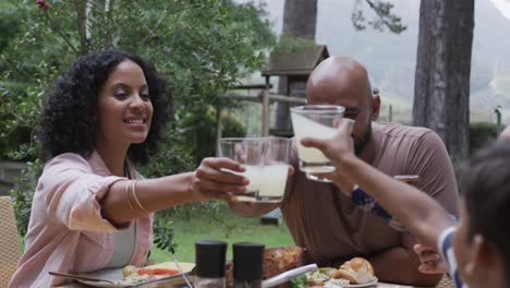 Happy-biracial-parents,-son-and-daughter-drinking-toast-at-dinner-table-in-garden,-slow-motion