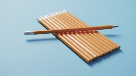 Close-up-of-pencil-on-row-of-pencils-with-blue-background,-in-slow-motion