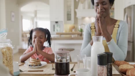 Happy-african-american-mother-and-daughter-praying-in-kitchen,-slow-motion