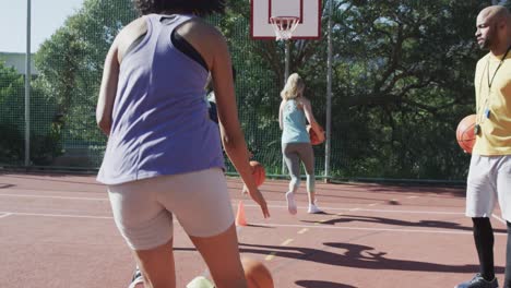 Happy-diverse-female-basketball-team-training-with-male-coach-on-sunny-court,-in-slow-motion