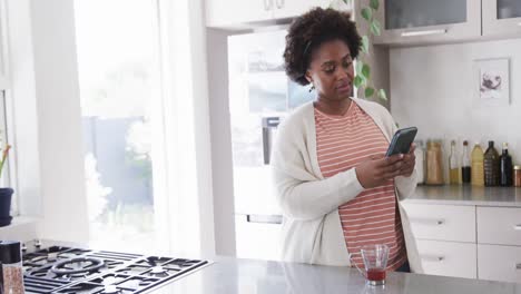 Mujer-Afroamericana-Enfocada-Usando-Un-Teléfono-Inteligente-Parado-En-La-Cocina-De-Casa,-Cámara-Lenta