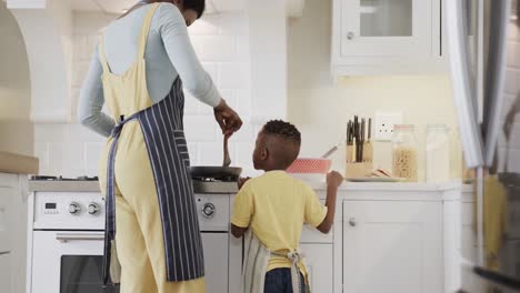 Happy-african-american-mother-and-son-frying-pancakes-in-kitchen,-slow-motion