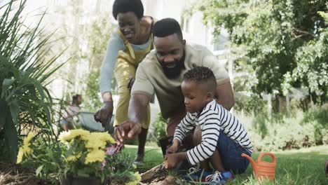 Happy-african-american-couple-with-son-planting-flowers-in-sunny-garden,-slow-motion