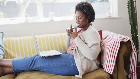 Fröhliche-Afroamerikanische-Frau,-Die-Auf-Der-Couch-Arbeitet,-Auf-Dem-Smartphone-Spricht-Und-Einen-Laptop-Benutzt,-Zeitlupe