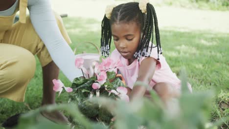 Glückliche-Afroamerikanische-Mutter-Und-Tochter-Pflanzen-Blumen-Im-Sonnigen-Garten,-Zeitlupe