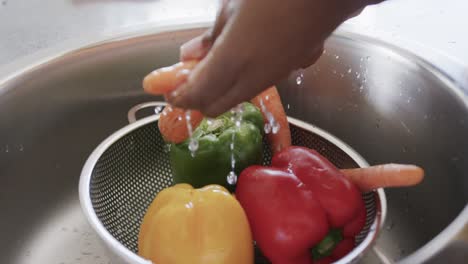 Close-up-of-hands-of-african-american-woman-rinsing-vegetables-in-kitchen-sink,-in-slow-motion