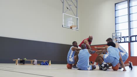 Diverse-male-basketball-coach-and-team-training,-stacking-hands-at-indoor-court,-in-slow-motion