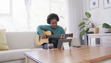 Feliz-Mujer-Afroamericana-Practicando-Tocar-La-Guitarra-Usando-Tableta-En-Casa,-Cámara-Lenta