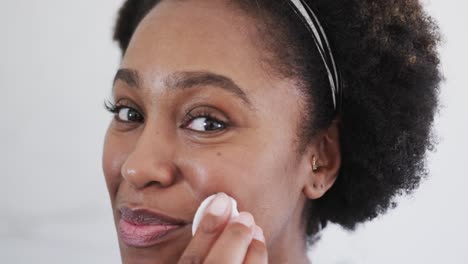 Close-up-of-happy-african-american-woman-cleansing-face-with-cotton-pad-in-bathroom,-slow-motion
