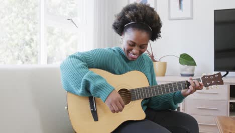 Feliz-Mujer-Afroamericana-Tocando-Guitarra-Y-Cantando-Sentada-En-El-Sofá-En-Casa,-Cámara-Lenta