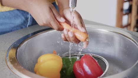 Midsection-of-african-american-woman-rinsing-vegetables-in-kitchen-sink,-in-slow-motion