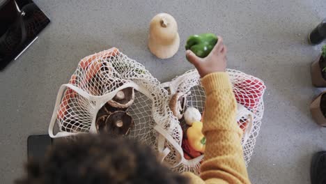 Overhead-view-of-african-american-woman-unpacking-groceries-in-kitchen,-in-slow-motion