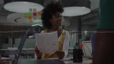 Animation-of-data-processing-over-african-american-woman-reading-a-document-to-her-colleagues