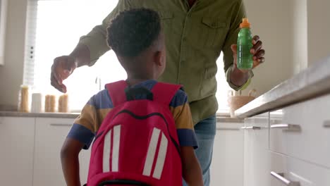 Happy-african-american-grandfather-embracing-with-grandson-in-kitchen-before-school,-slow-motion