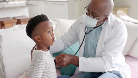 Senior-african-american-male-doctor-in-face-mask-using-stethoscope-on-boy-patient,-slow-motion