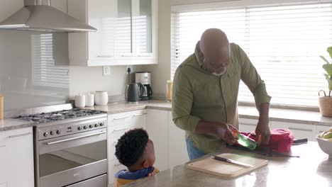 African-american-grandfather-packing-schoolbag-for-grandson-in-kitchen-before-school,-slow-motion