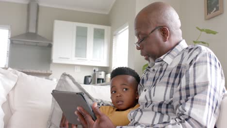 Afroamerikanischer-Großvater-Mit-Enkel,-Der-Zu-Hause-Ein-Tablet-Auf-Der-Couch-Benutzt,-Zeitlupe