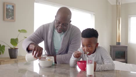 Happy-african-american-grandfather-having-breakfast-with-grandson-in-kitchen,-slow-motion